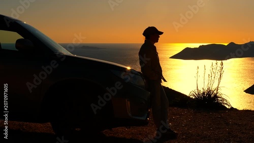 Man enjoying a relaxing road trip sunset by the sea. Solitary man's silhouette standing next to his car on a scenic overlook, peacefully contemplating a beautiful golden sunset reflecting on the sea