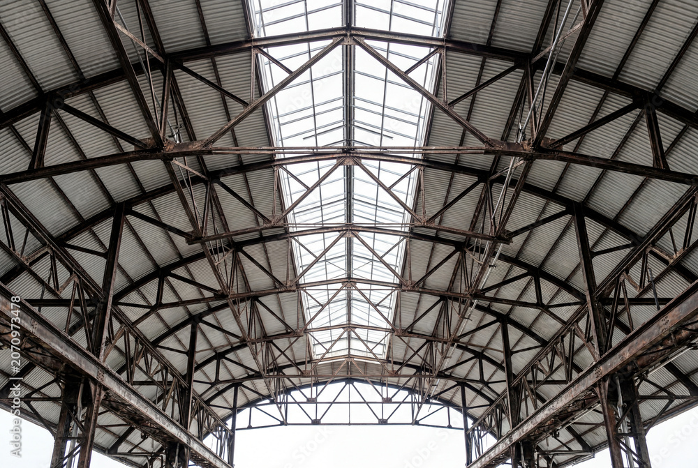 Fototapeta premium Low angle view looking up at the complex metal trusses and skylights of a vast industrial roof