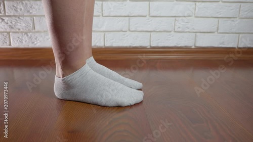Female feet performing calf raise exercise. Woman performing calf raises in grey socks on a wooden laminate floor, strengthening her leg muscles with a simple home workout fitness routine