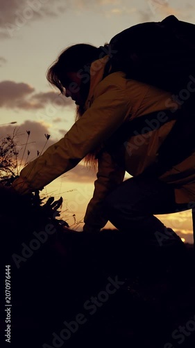 Silhouette of woman climber with backpack against sky, climbing to top of hill. Victory success in business. Hiker. Traveler woman climbs to top of rock. Striving for success, achievement in business