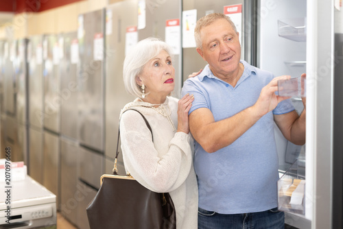 Obraz na plátně Elderly couple stands in a hardware store and chooses a roomy refrigerator to st
