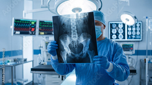Bild auf Leinwand Male surgeon in blue scrubs holding an x-ray film of a human pelvis in a modern