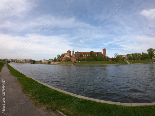 The green bank of Vistula river with The Wawel Royal Castle and Cathedral Basilica in the background, Krakow, Poland. Tourist boats on Vistula river.