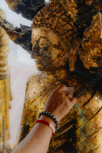 фотографія BANGKOK, THAILAND, 5 October 2025 – A devotee applies gold leaf to a Buddha statue at Wat Phra, a significant Buddhist temple in Bangkok