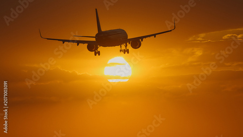 Schilderij op canvas Airplane descending against a vibrant sunset sky with dramatic clouds