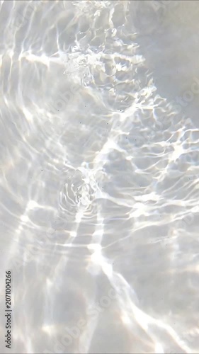 Caustic light patterns reflecting on a white background with drops creating ripples in the clean water surface