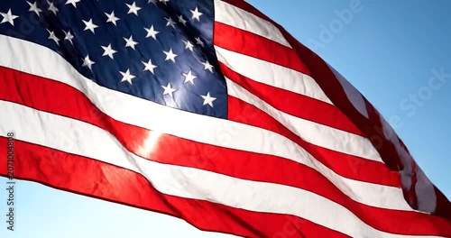 American flag waving in the wind against a clear blue sky with sun flare.