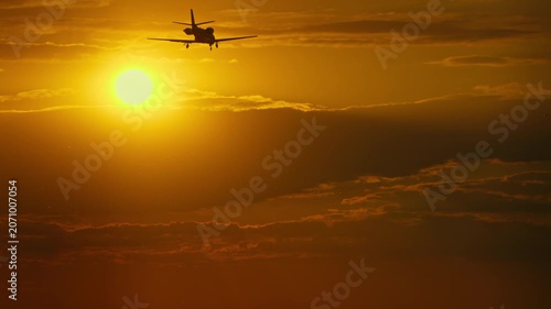 Small jet airplane flying against a vibrant sunset sky with clouds