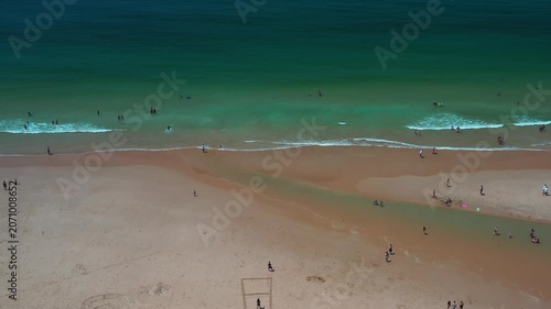 A beach near Caparica in Portugal. People are swimming and relaxing on the sand. The waves crash gently on the shore. Families enjoy their time together.