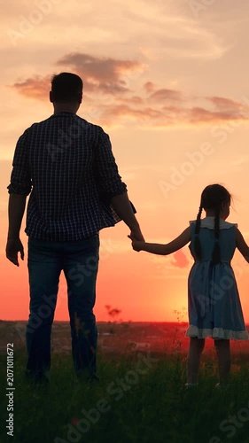 Papa, kid daughter admire sunset together. Young daughter holds her dad hand in meadow, sunset sky. Family trip. Father, child daughters enjoy freedom, dream at dawn. Dad, child holding hands in park