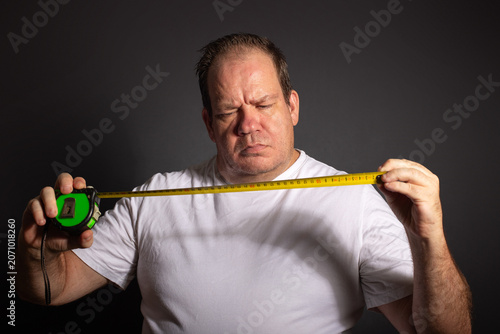 Confused man measuring himself with tape measure and concerned expression