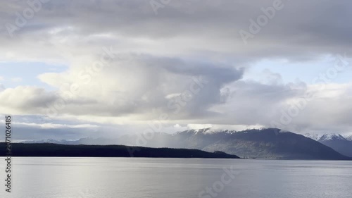 A dramatic cloudburst trails rain over snowy peaks and a headland