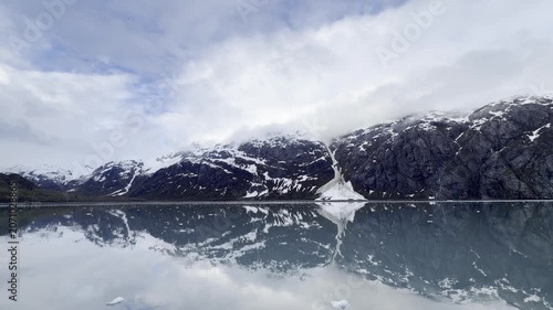 Cloud-capped peaks double on glassy pale-green water as light breaks