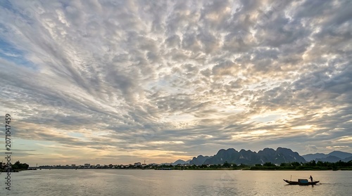 Fisherman rowing a boat on a calm river under dramatic sunset clouds