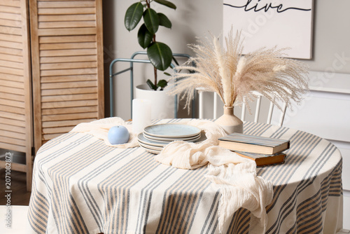 Photos Vase with pampas grass, dishes, books and candles on dining table in room