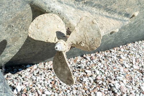 Cuadro en lienzo Old weathered bronze boat propeller resting on a pebbly beach shore, abandoned maritime equipment, coastal concept