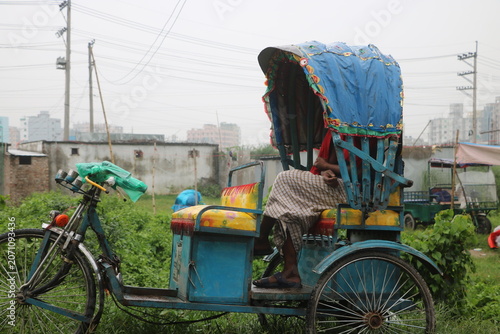 Traditional tricycle rickshaw parked in green grassy field with three wheeler