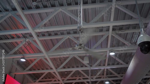 Handheld shot captures a large industrial fan in motion inside a warehouse, its spinning blades filling the frame against a gray ceiling structure background in a clean neutral industrial setting