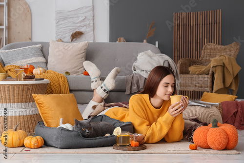 Young woman with cup of tea and cute British cat lying at home on autumn day