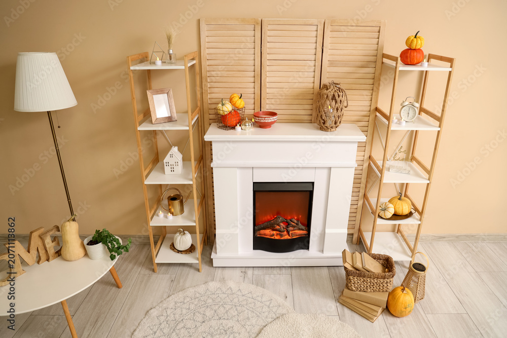Obraz premium Interior of stylish room with shelving units, table and autumn decorations on modern fireplace near beige wall
