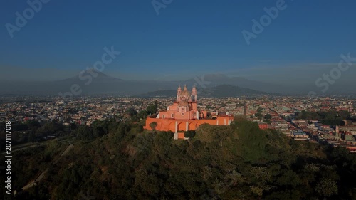 Drone panoramic rotation around the Church of Cholula built on top of the ancient pyramid with San Pedro Cholula town and Popocatepetl and Iztaccihuatl volcanoes at sunset