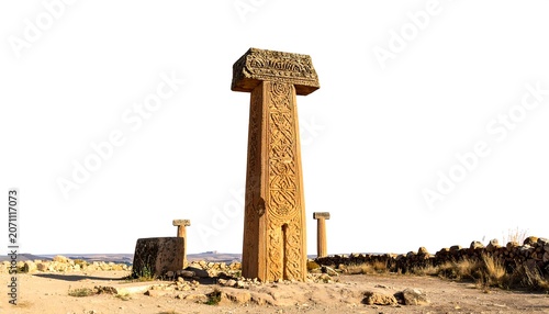 A tall, weathered stone monument stands on a plain with a few others and a wall in the background. The sky is white