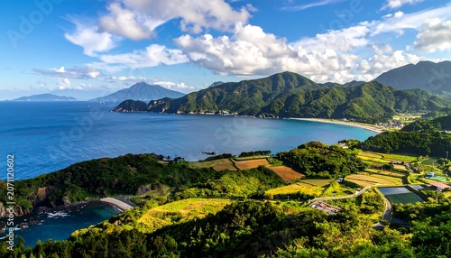 A sweeping vista of a coastline featuring a blue ocean, distant mountains, lush green hills, and fluffy white clouds