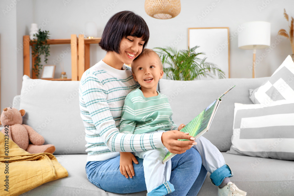 Naklejka premium Young mother with her little son reading story on sofa at home