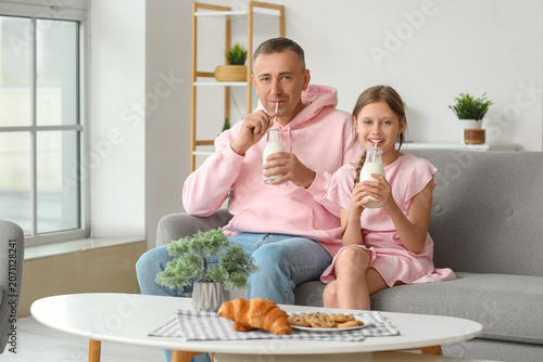 Fotografie Little girl and her father with pastries drinking milk in living room