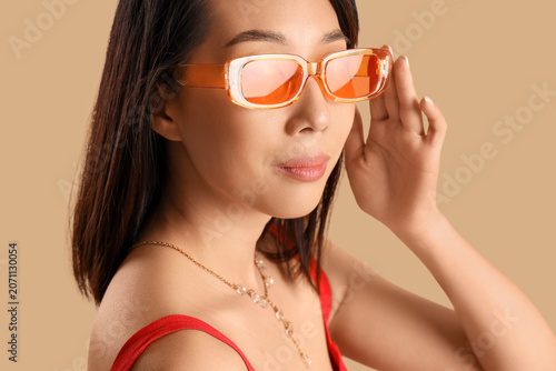 Beautiful Asian woman in stylish sunglasses on beige background, closeup