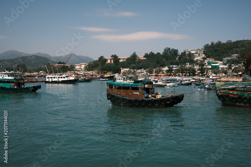 View of traditional sampan boats and vessels anchored in the harbor with lush hills and buildings in the background in Hong Kong, Hong Kong.