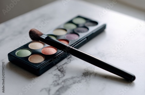 Vibrant eyeshadow palette and makeup brush on a marble surface, close-up shot.