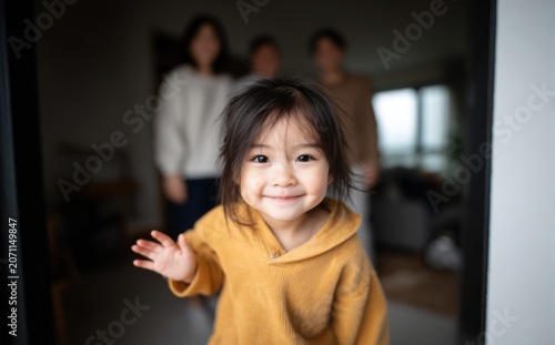Happy Little Asian Girl Waving Hello with Family in Background at Home