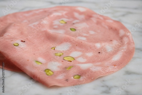 Slice of mortadella with pistachio pieces on marble surface, close-up.