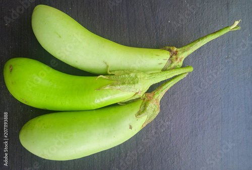 three green eggplants isolated on a dark wooden background, photographed from above