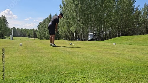 Swinging a golf club on a sunny day at a golf course with trees in the background and a clear sky