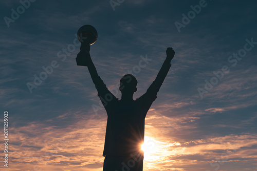Man holding trophy in sunset silhouette.