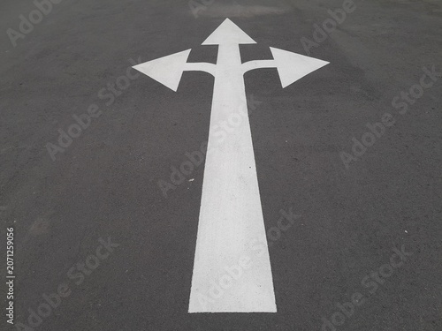 close up photo of a road traffic sign in the form of a white arrow painted on an asphalt surface.