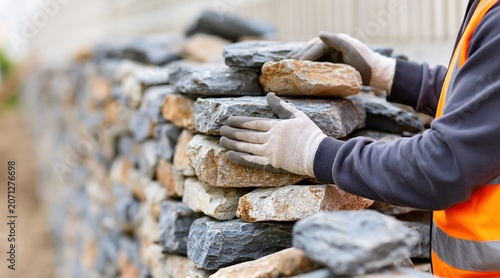 Close up of worker building dry stone wall with natural stones