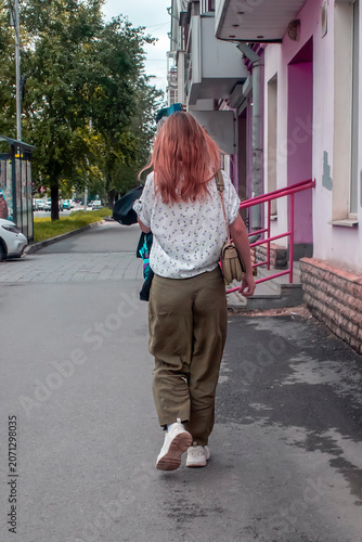 A woman with a shoulder bag walks along the sidewalk on a summer day
