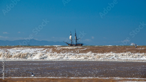 Wooden tall ship which is a full-scale 18th-century brig replica sailing through white-capped waves along the California coastline near Ventura, United States