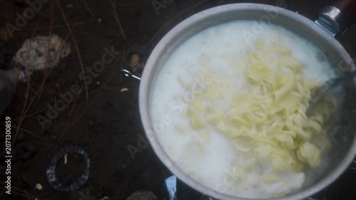 Preparing instant noodles in a pot over a campfire during a camping trip providing a quick and easy meal outdoors for adventurers and nature enthusiasts