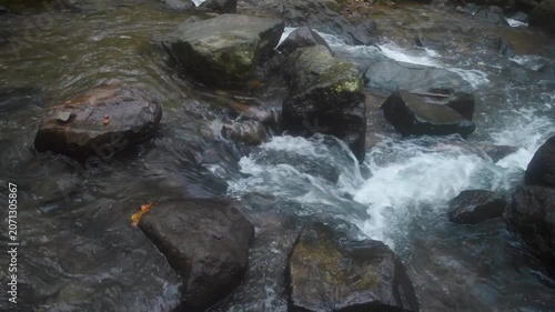 Clear water flows rapidly over rocks in a tropical stream within a lush Indonesian landscape, showcasing the power and beauty of nature's waterways and mountain environments