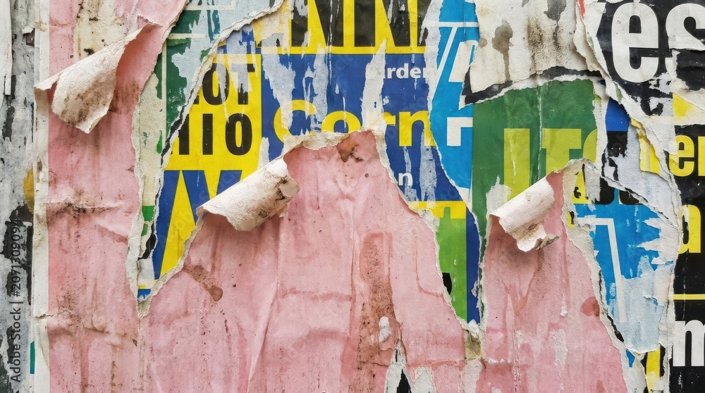 Fototapeta premium Close-up of a wall covered with layers of torn, weathered, and colorful advertising posters.