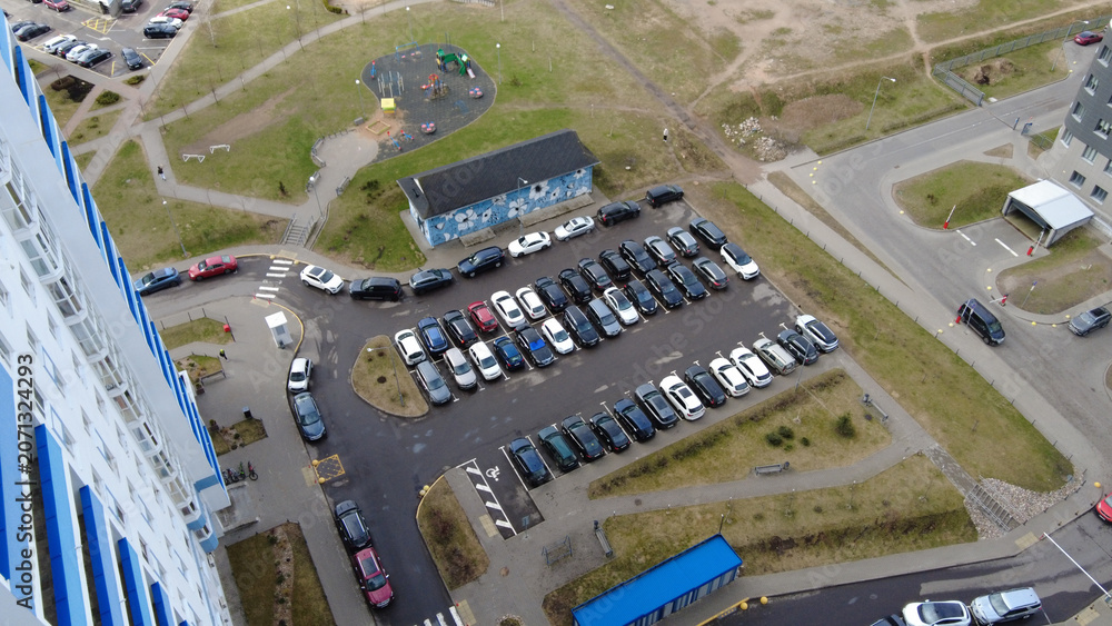 Fototapeta premium Parking lot filled with cars near playground and buildings in a residential area during daytime