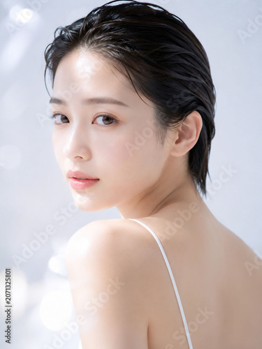 淡いライトグレー背景で肩越しに振り向く濡れ髪風の若い女性が透明感ある素肌を見せる高級感あるスキンケア美容ポートレート