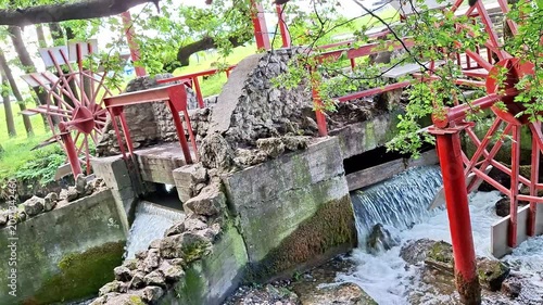 Water flows through a mill sluice and spillway surrounded by stonework and greenery. Cascading currents, textured surfaces, and peaceful outdoor scenery create a calming atmosphere