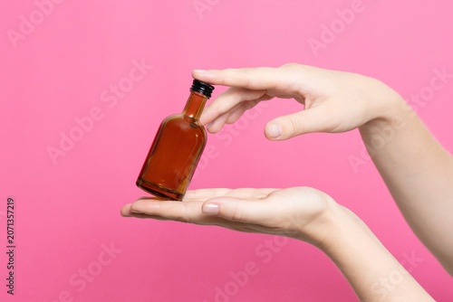 Hands holding tiny glass bottle on pink background