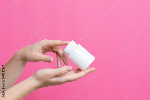 Hands holding white pill bottle on pink background