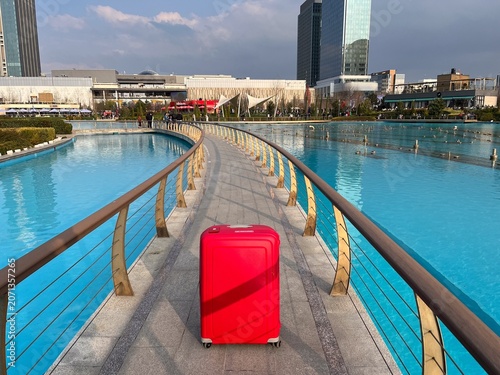 Red suitcase standing on pedestrian bridge over water